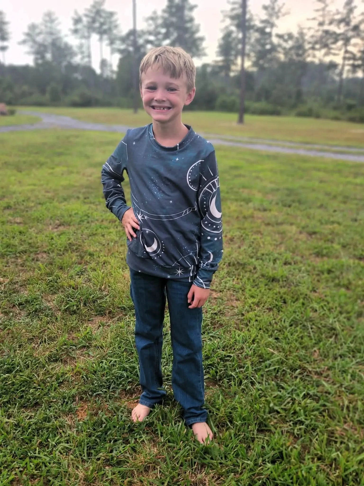 A boy smiles in a long-sleeved shirt with a celestial sky and moon pattern.