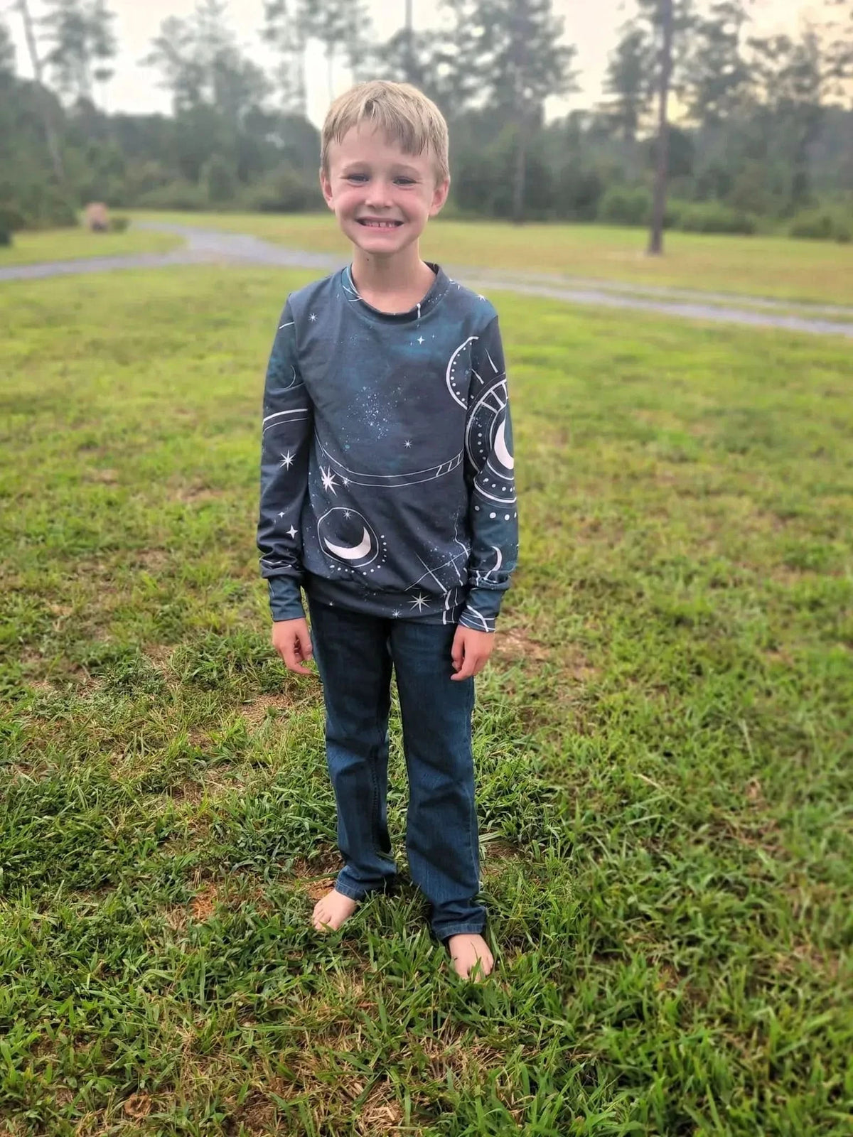 A boy wears a long-sleeved shirt with a celestial sky and moon pattern.