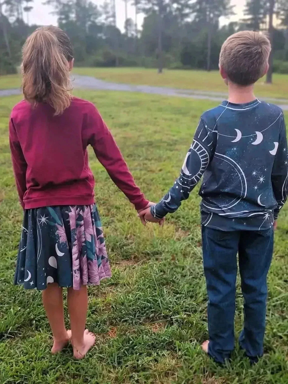 A girl in a celestial sunflower skirt holds hands with a boy in a matching shirt.
