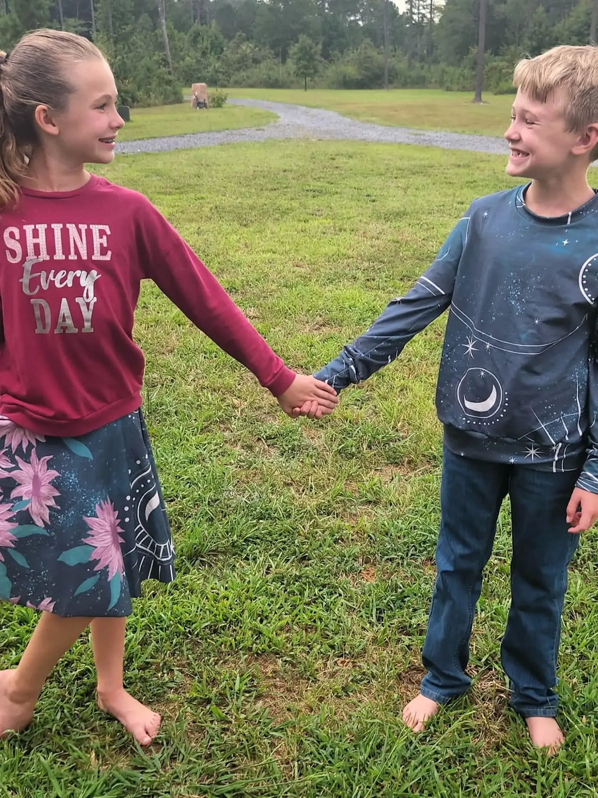 A girl in a sunflower skirt and a boy in a celestial shirt hold hands outdoors.