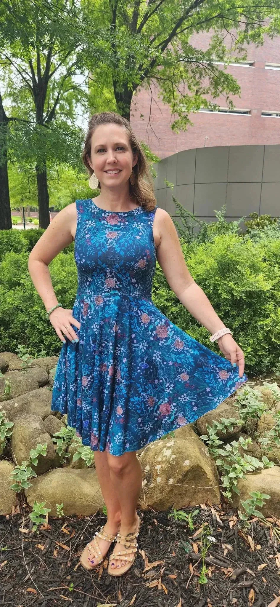 A woman in a teal woodland print dress stands outdoors.