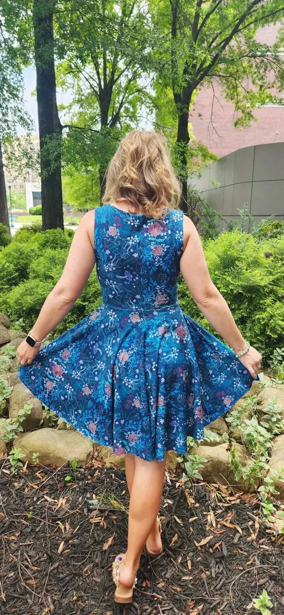 Rear view of a teal woodland print dress with floral accents, worn by a woman outdoors.