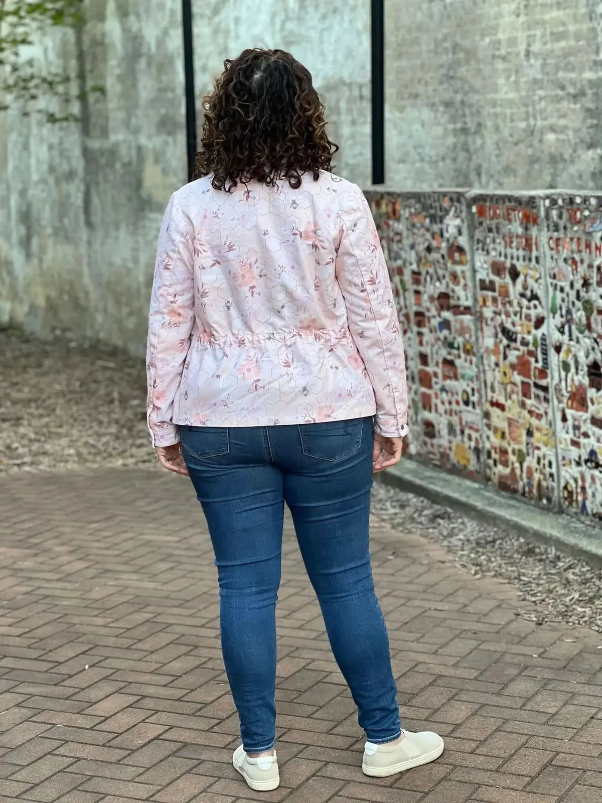 A woman from behind wears a peach jacket with a garden bee pattern and blue jeans.