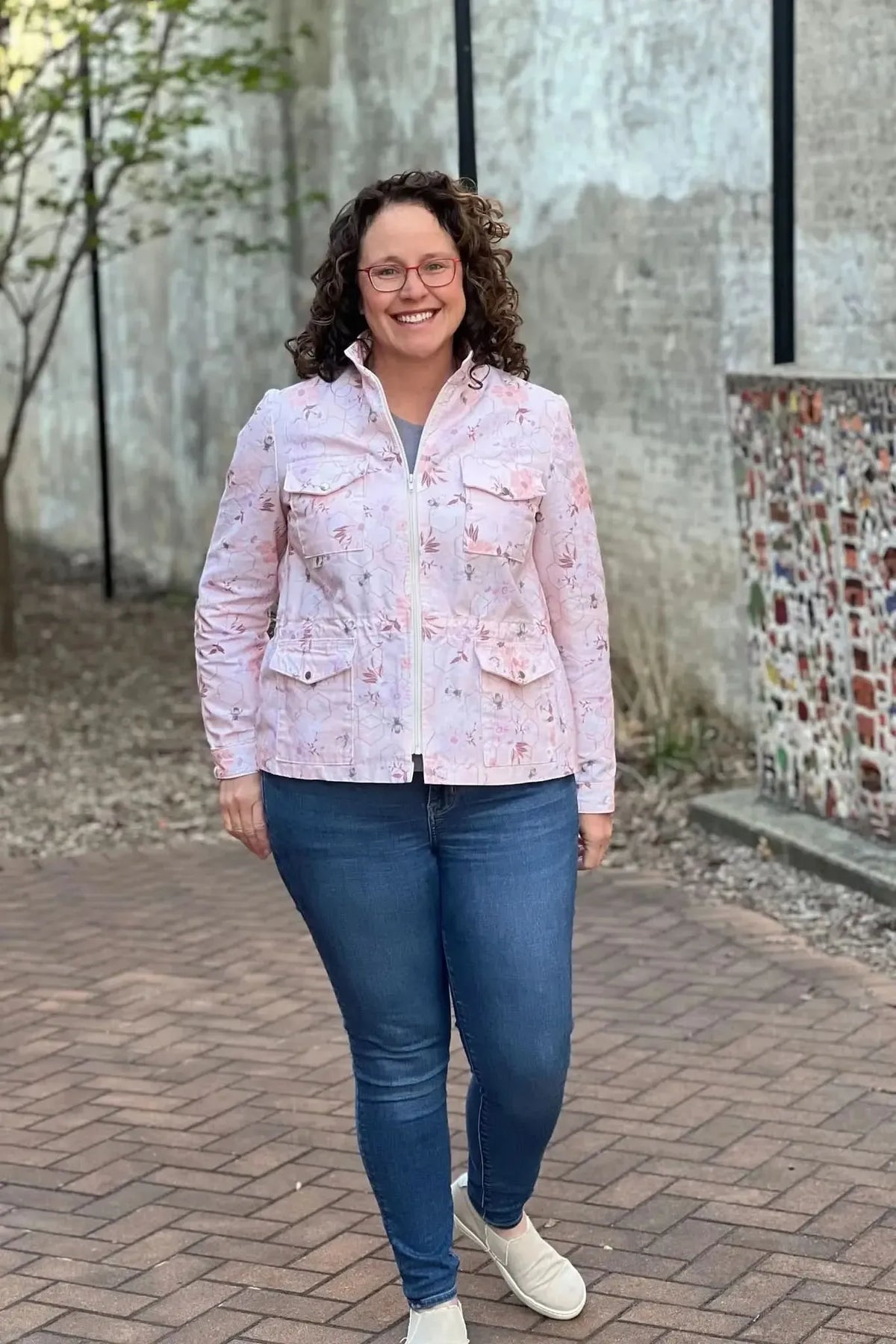 Woman in a peach jacket with a garden bee pattern, blue jeans, and white shoes.