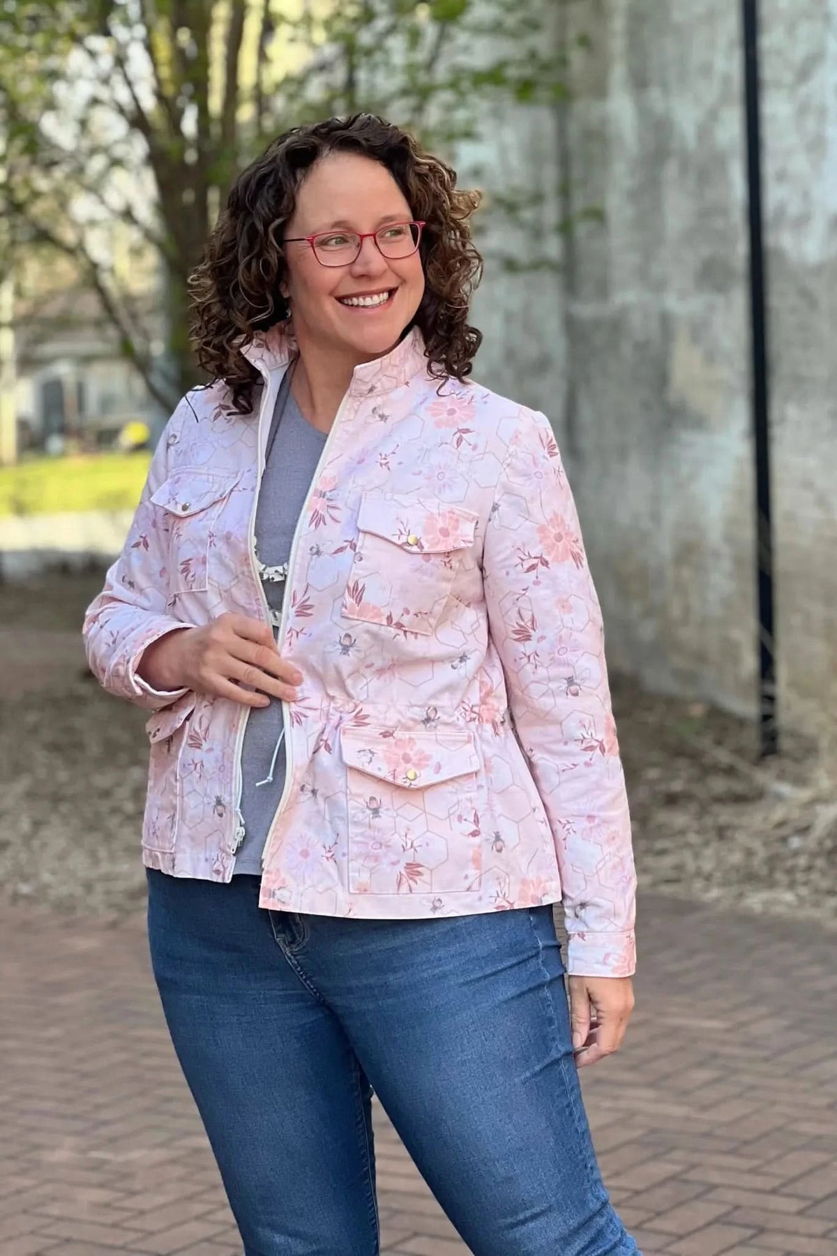 Woman in a peach floral and bee print jacket with a gray shirt and jeans.