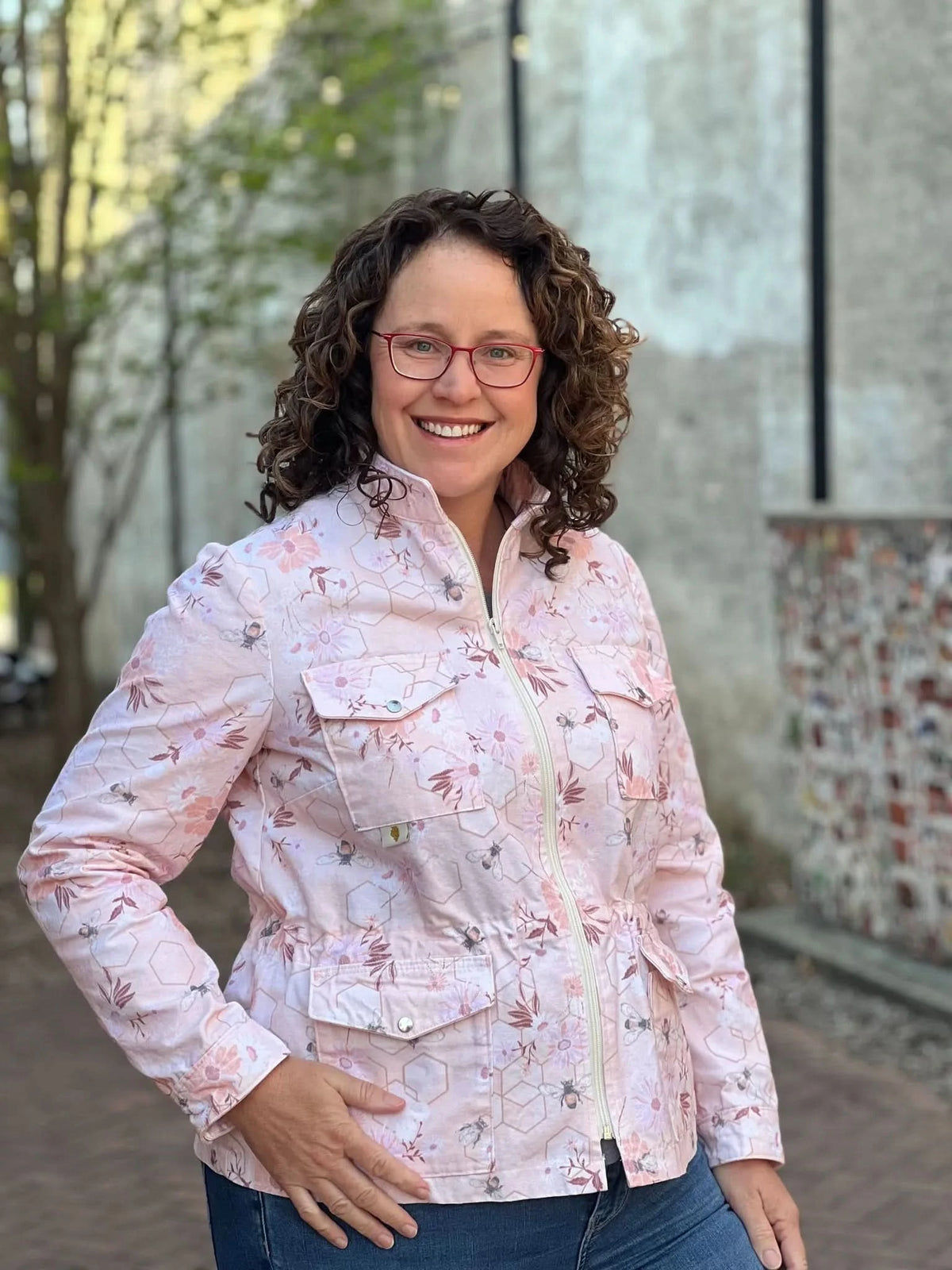 Woman in a peach floral and bee print jacket with red glasses.