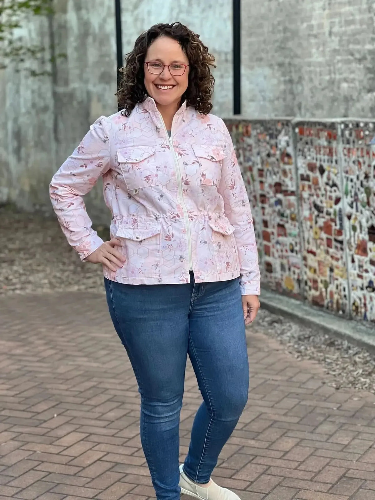 A woman smiles wearing a peach floral and bee print jacket with jeans.