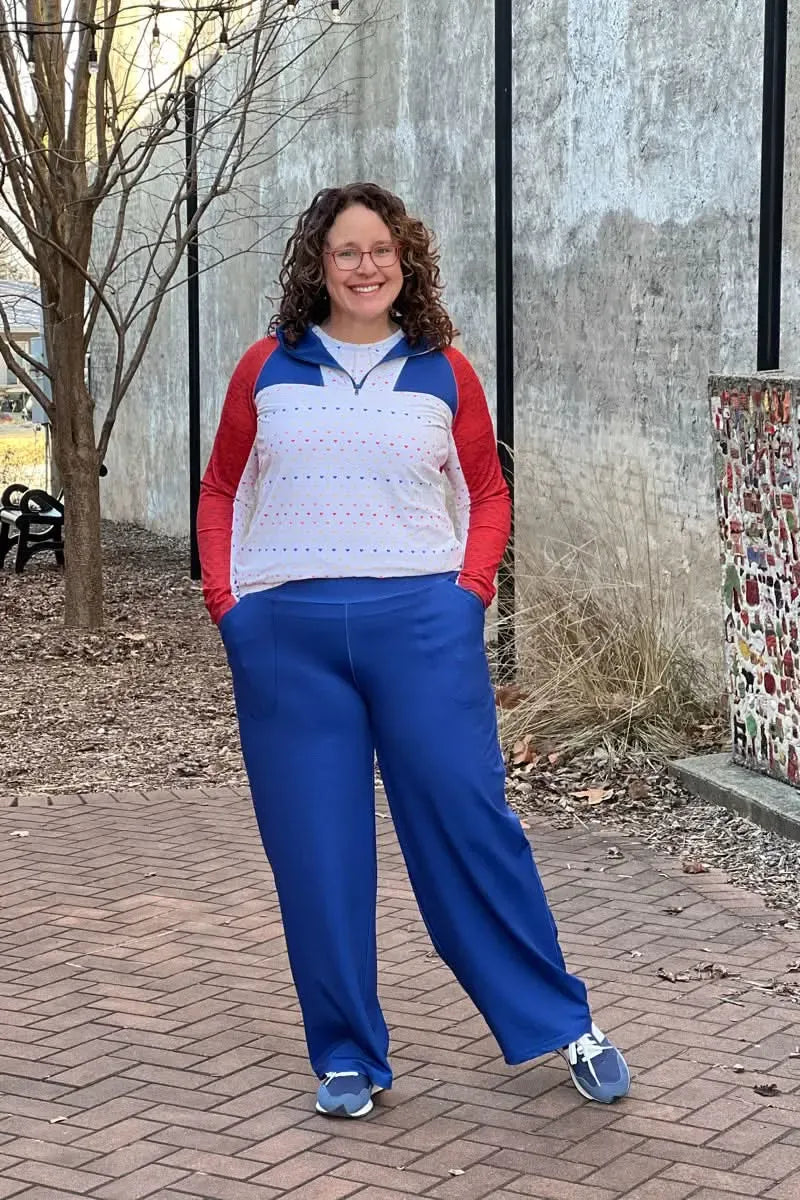 A woman smiles, wearing a blue and red top with blue pants and sneakers.