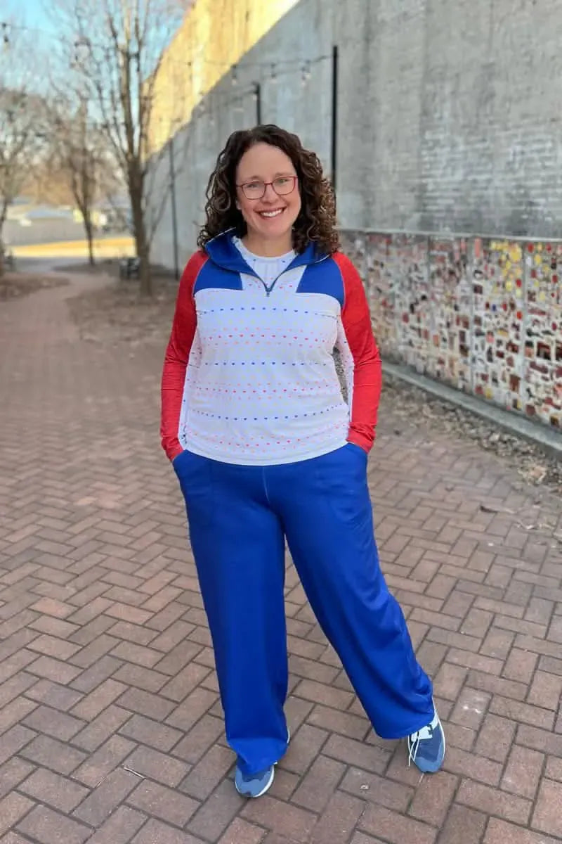 A woman wears a blue heather top with red sleeves and blue pants.