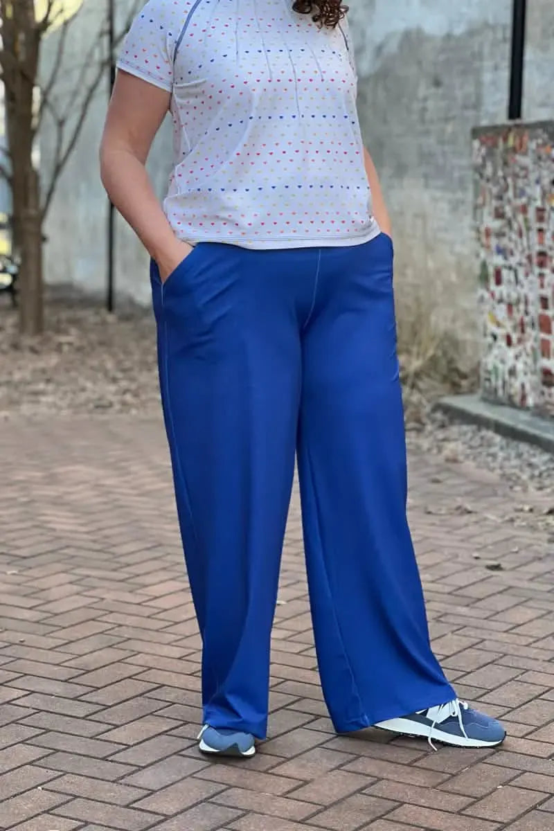A person wears a white shirt with colorful hearts and blue wide-leg pants.