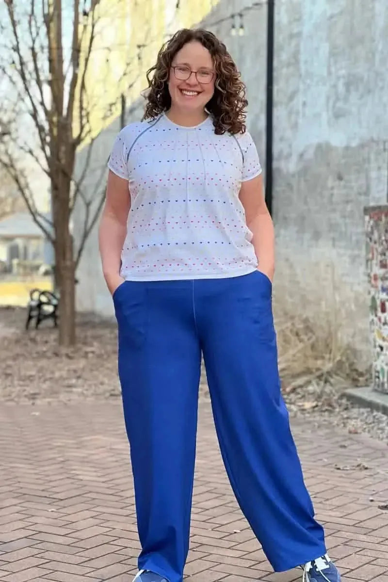A woman smiles, wearing a white top with blue and red hearts and blue pants.