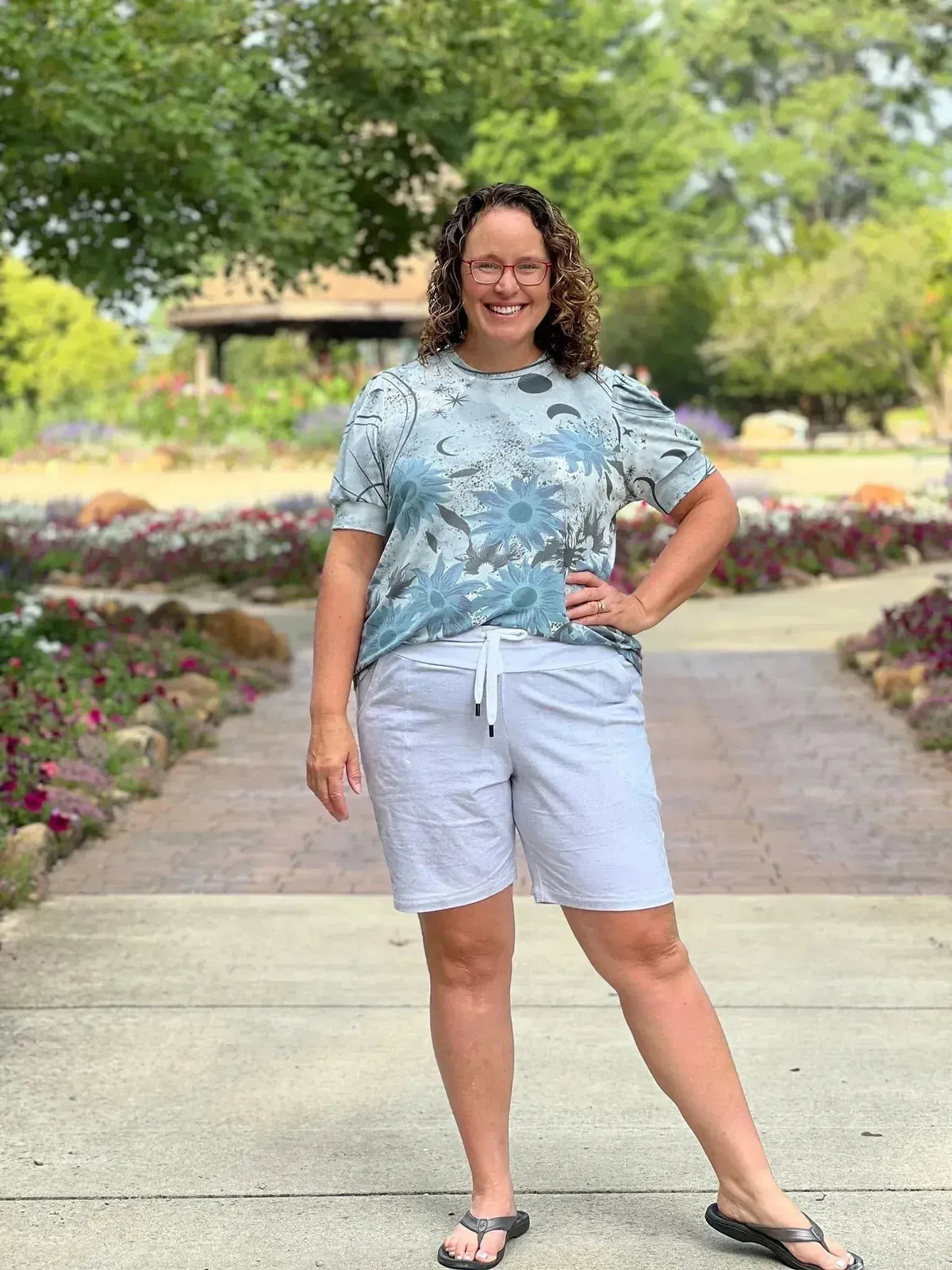 A woman wears a light blue celestial moon and stars print t-shirt and light gray shorts.
