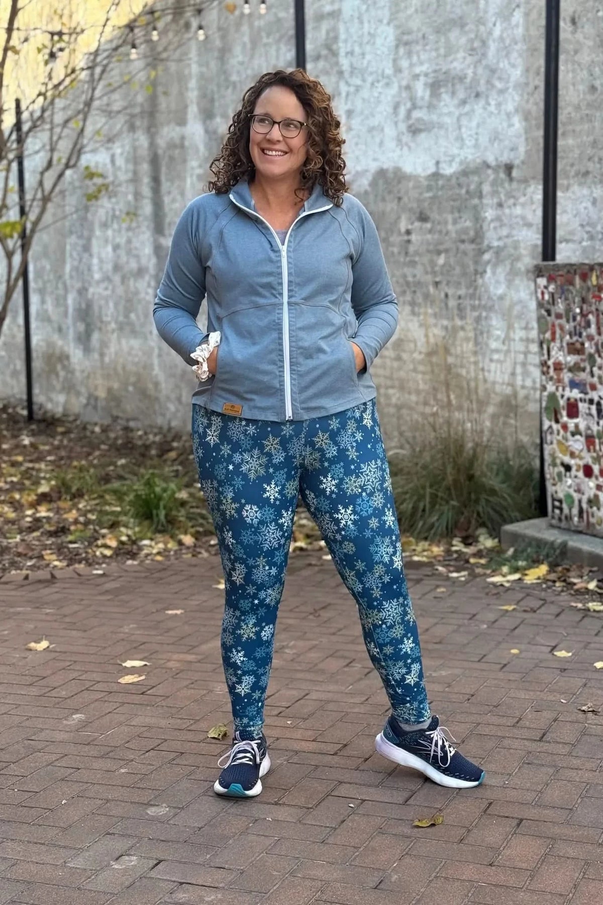 A woman smiles, wearing a blue zip-up jacket and snowflake-patterned leggings.