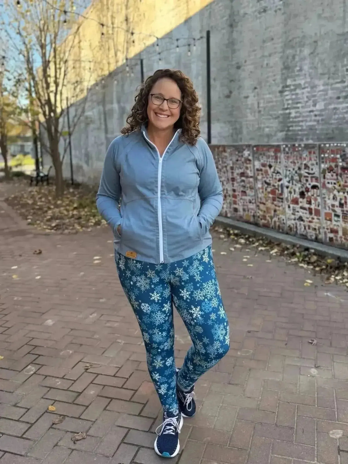 Woman wearing light blue zip hoodie and snowflake-print leggings outdoors.