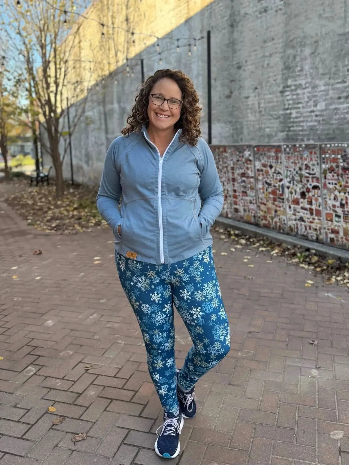 Woman wearing light blue zip hoodie and snowflake-print leggings outdoors.