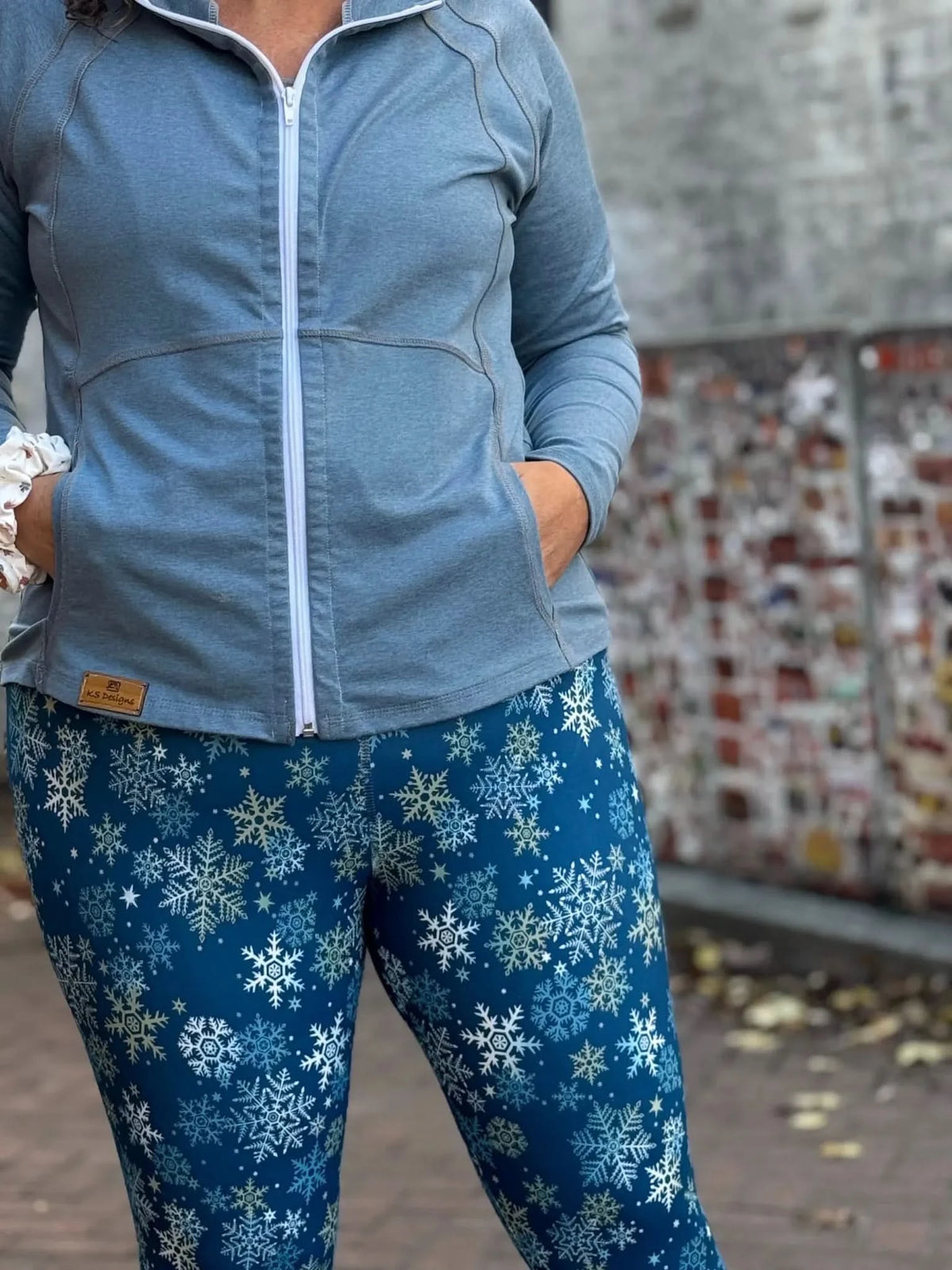 A person wears a blue zip-up jacket and blue leggings with white snowflakes.
