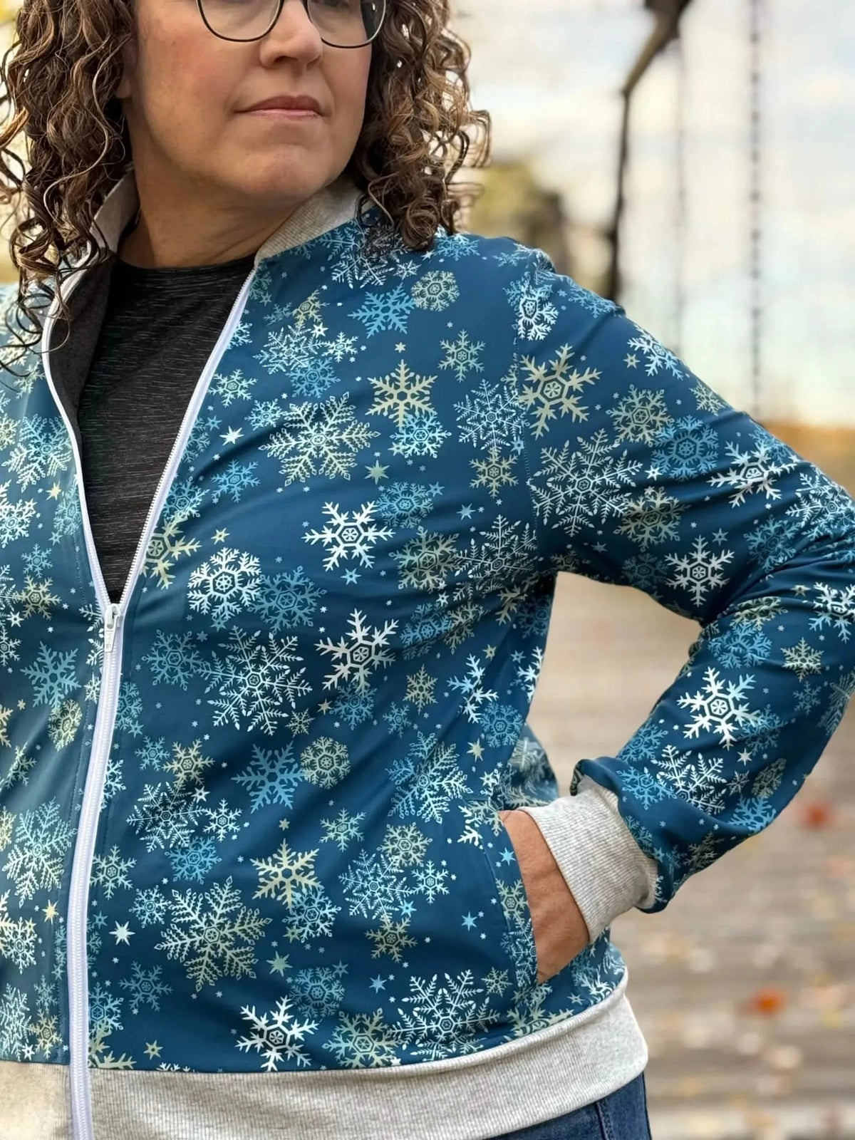 A woman wears a blue jacket with a white snowflake pattern and gray cuffs.