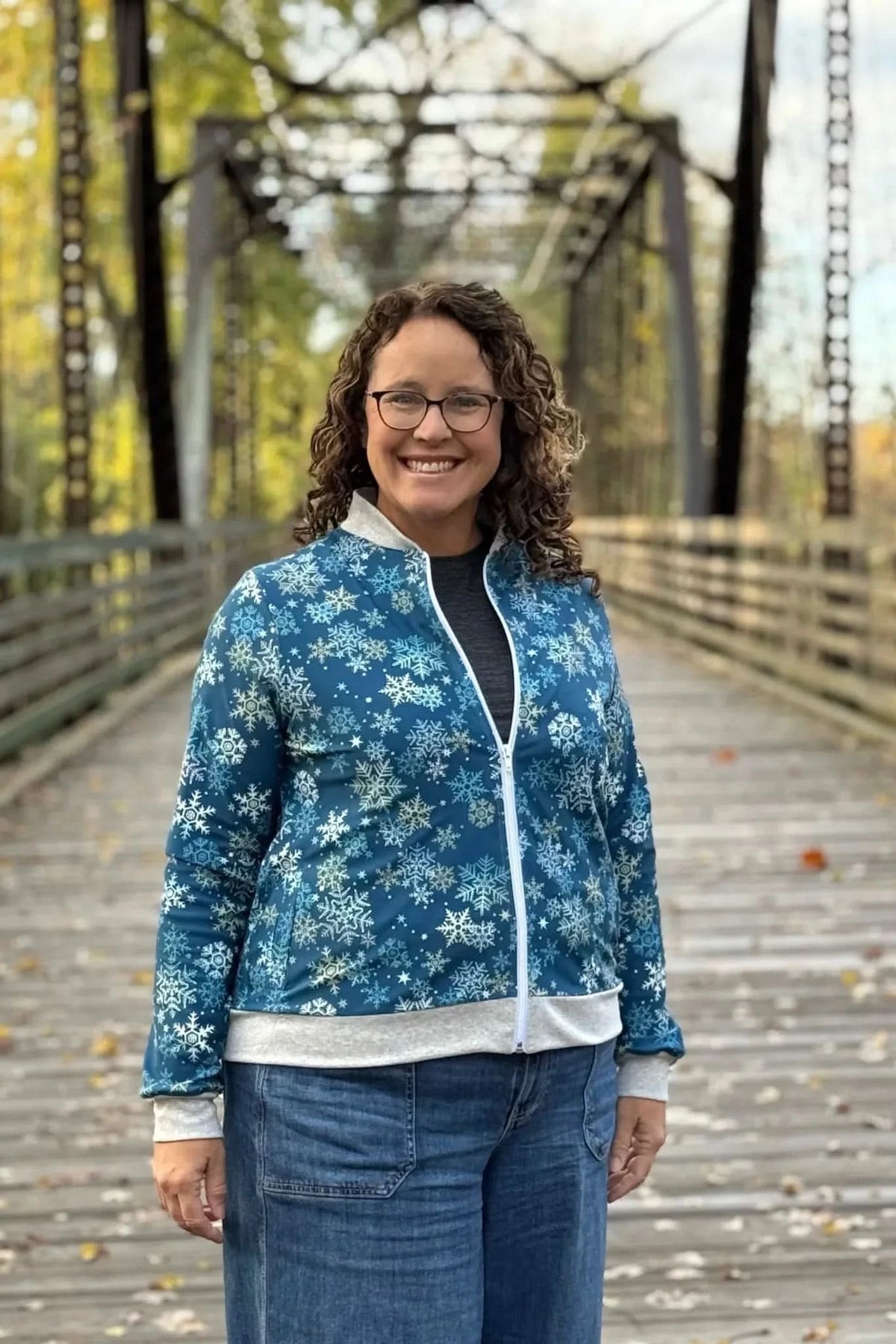 A woman smiles wearing a blue snowflake-patterned jacket with a white zipper and gray trim.