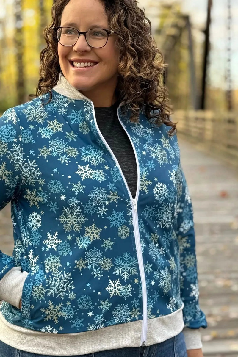 A woman smiles, wearing a blue snowflake-patterned jacket with a white zipper.