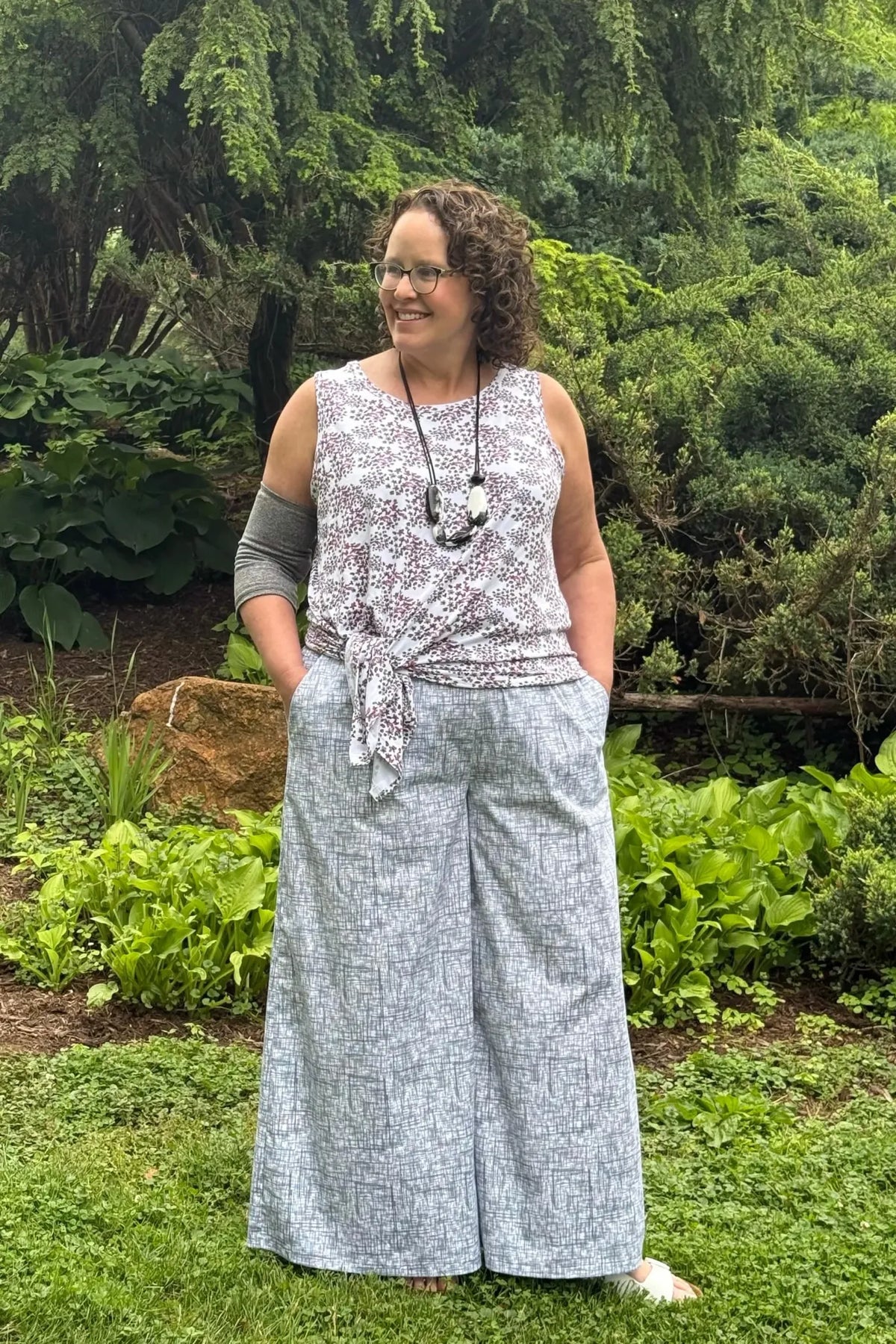 Woman in a black hatch print tank top and wide-leg pants, standing in a garden.