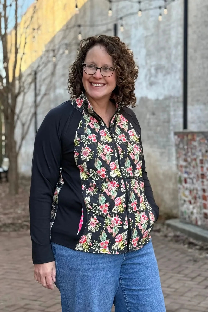 A woman smiles, wearing a black jacket with a floral print and blue jeans.