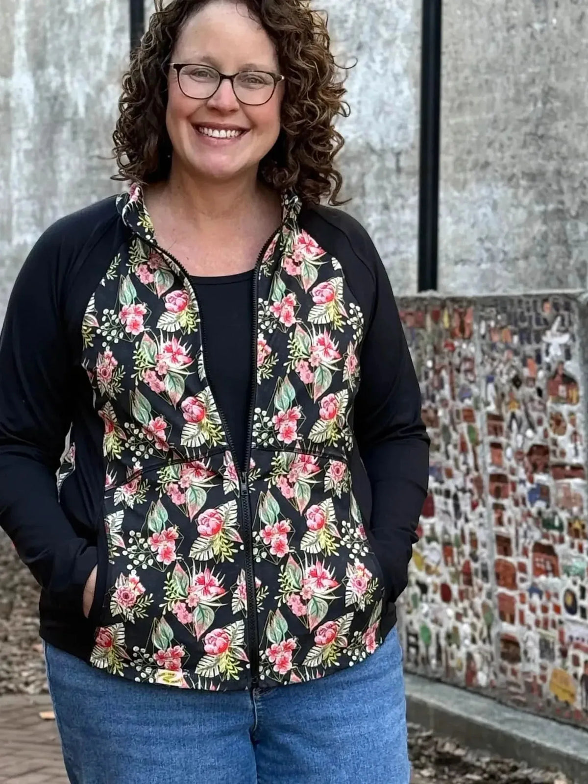 A woman smiles wearing a black jacket with a pink and green floral pattern.
