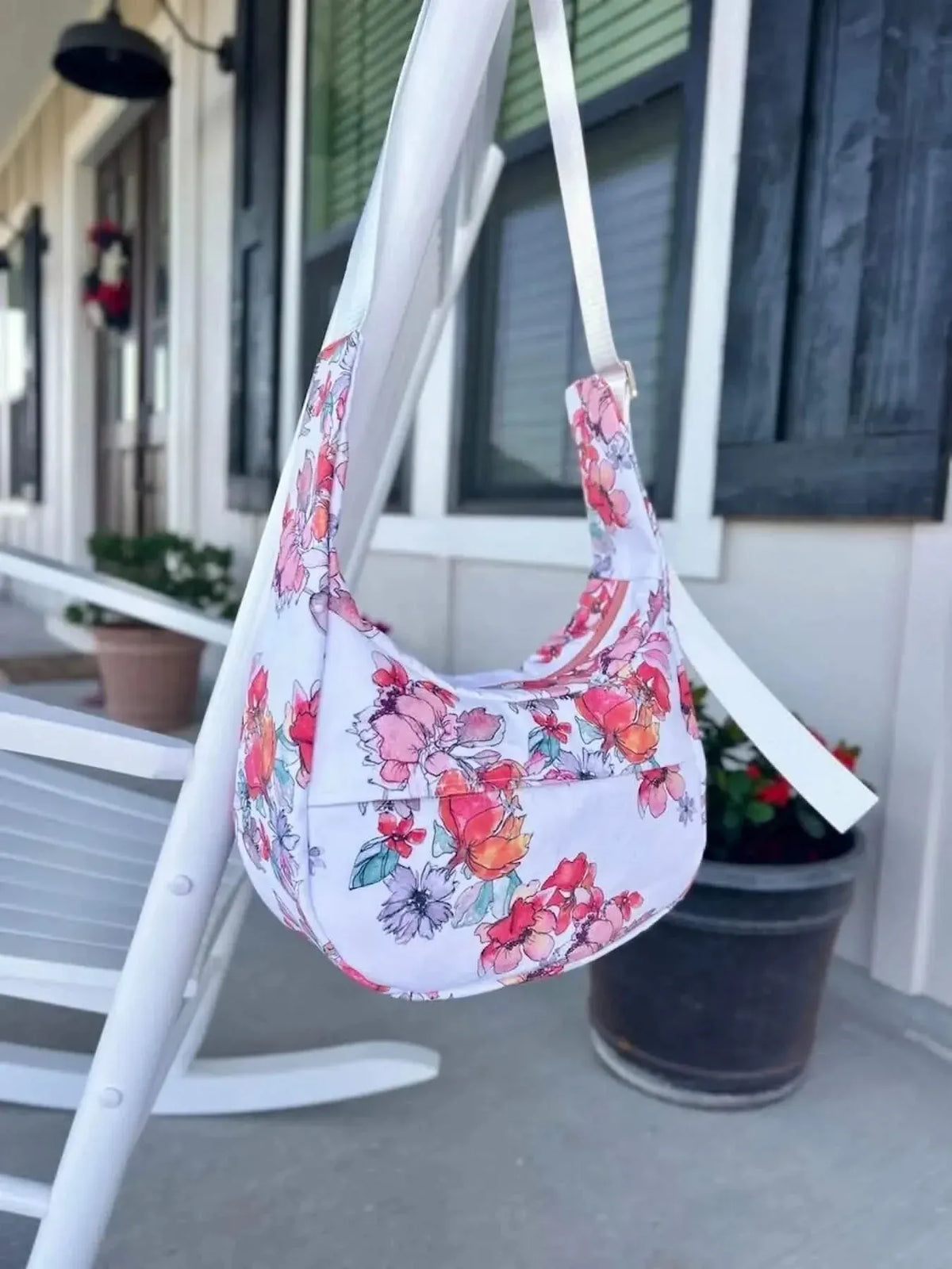 A floral print fabric bag hangs from a white porch swing.