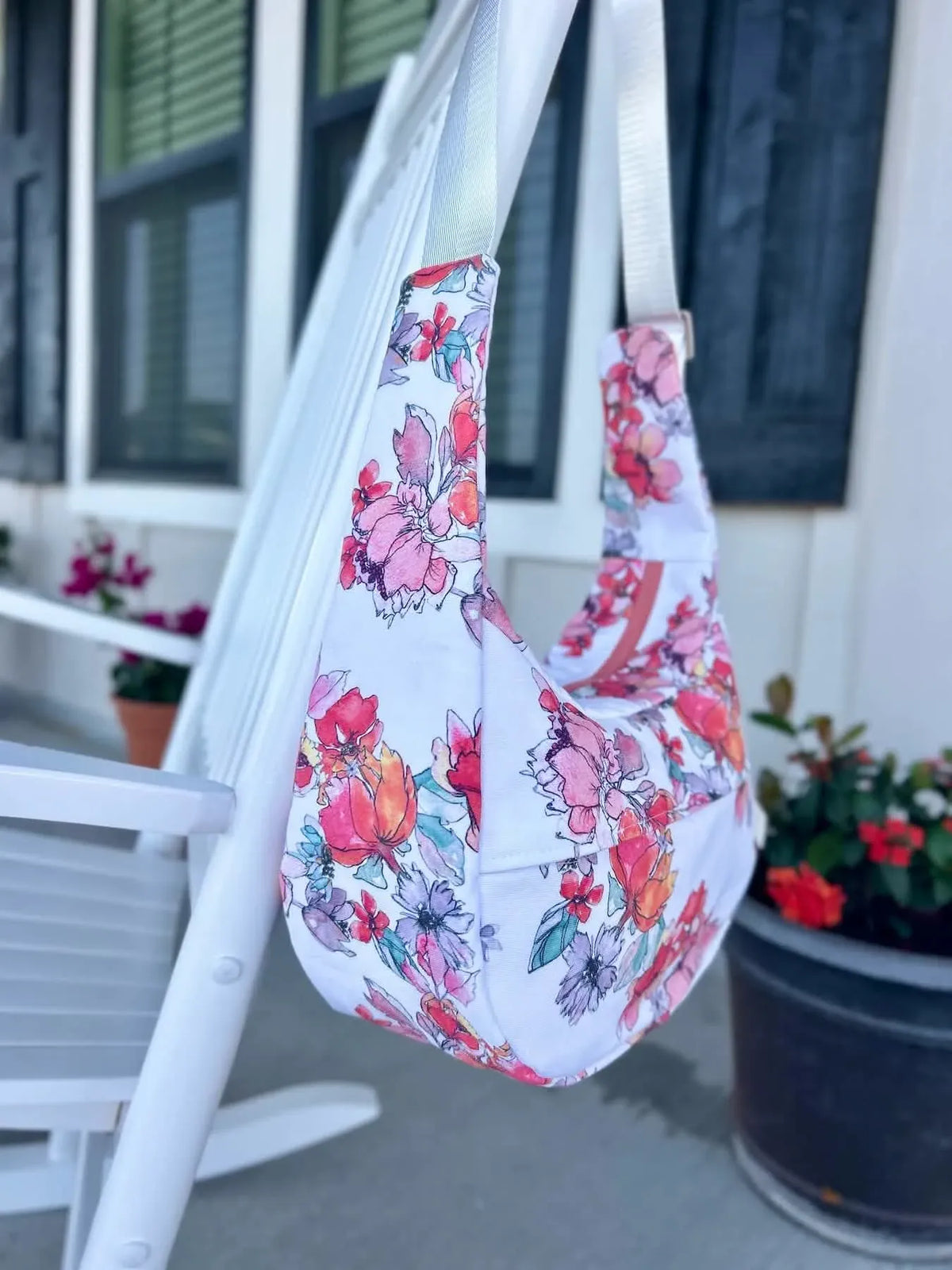 A floral fabric bag with pink, orange, and purple flowers hangs on a white chair.