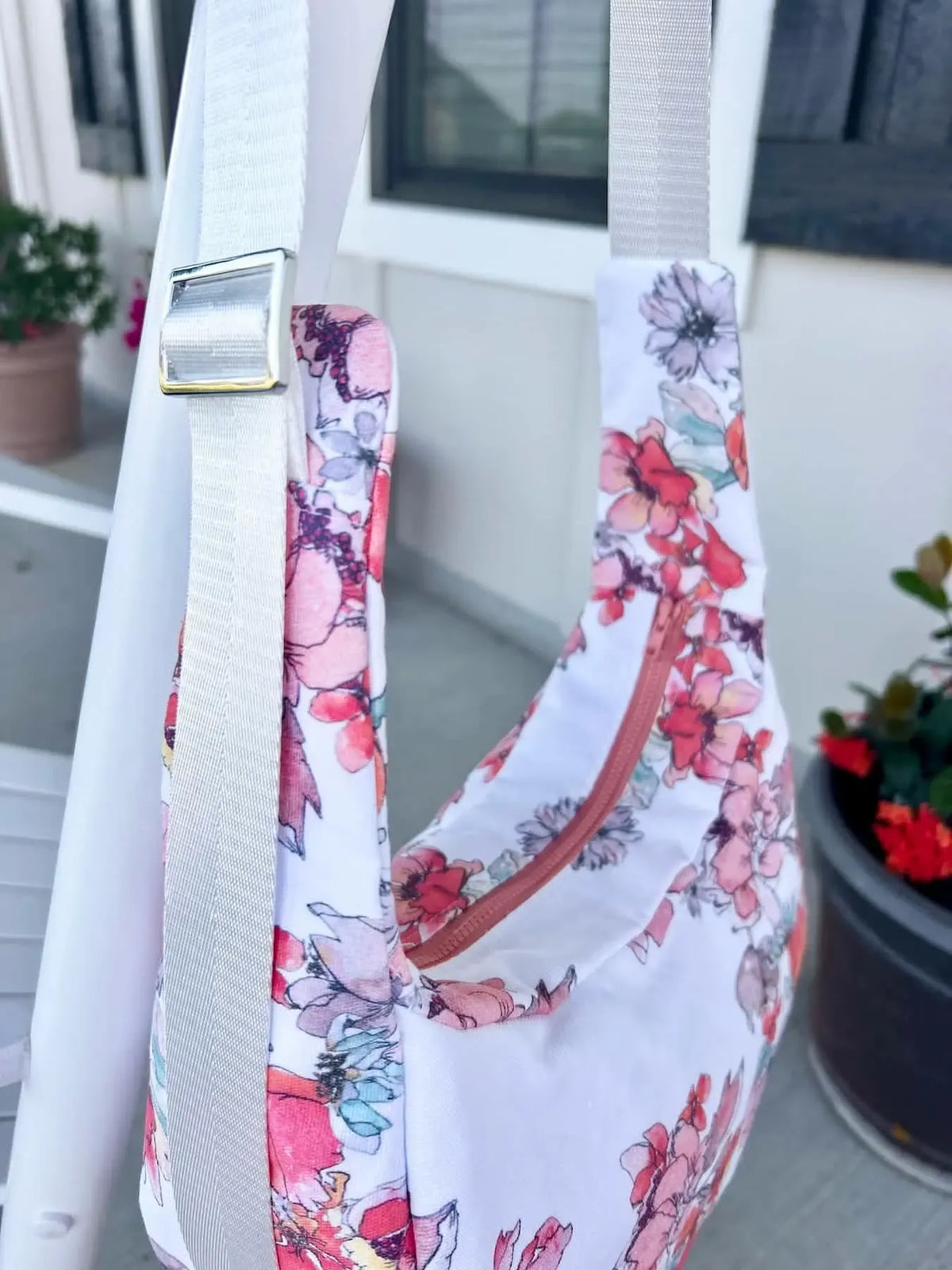 A floral fabric bag with a white strap and a rose gold zipper.