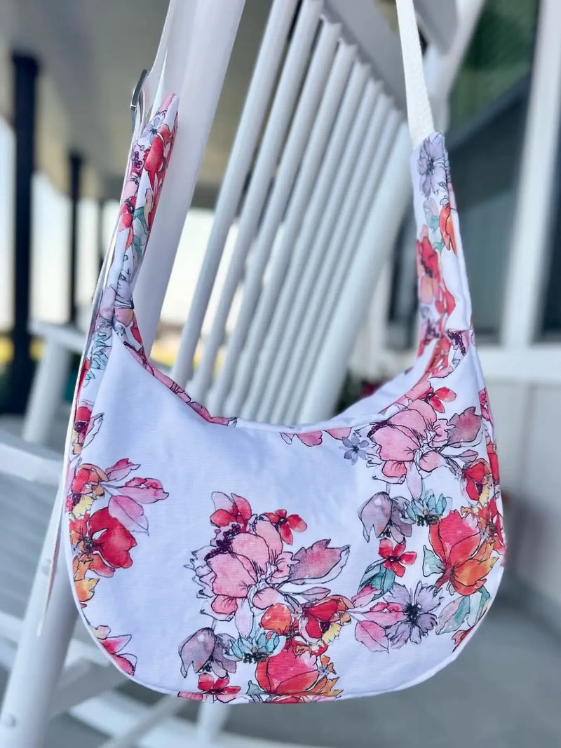 A white floral print bag with pink, red, and orange flowers hangs on a white chair.
