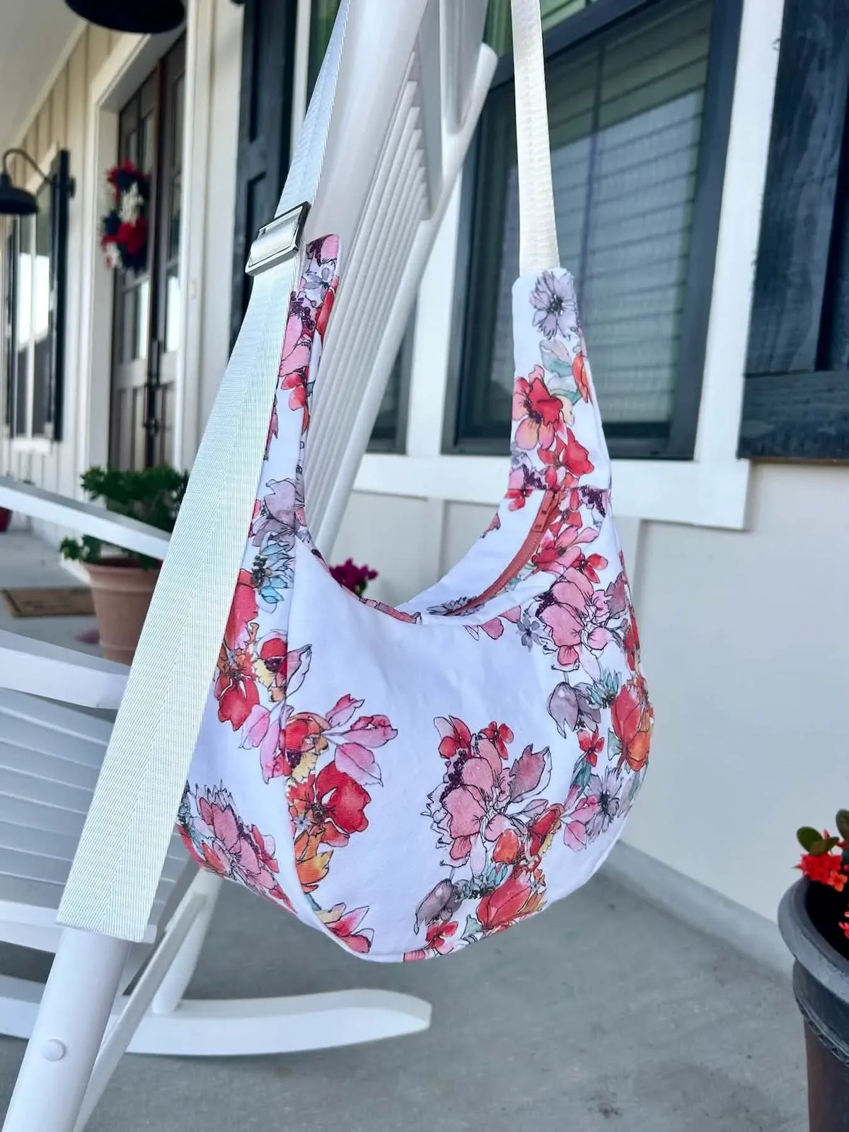 A white floral bag with red and pink flowers hangs on a white chair.