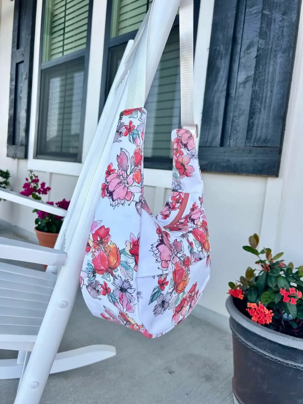 A floral print fabric bag hangs from a white porch swing.