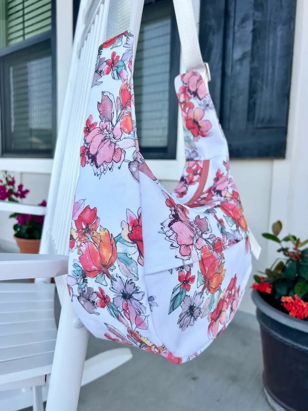 A floral print fabric bag hangs on a white chair.