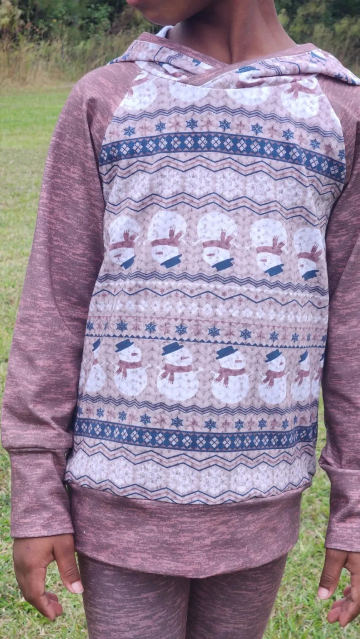 A child wears a long-sleeved shirt with a snowman and snowflake pattern.