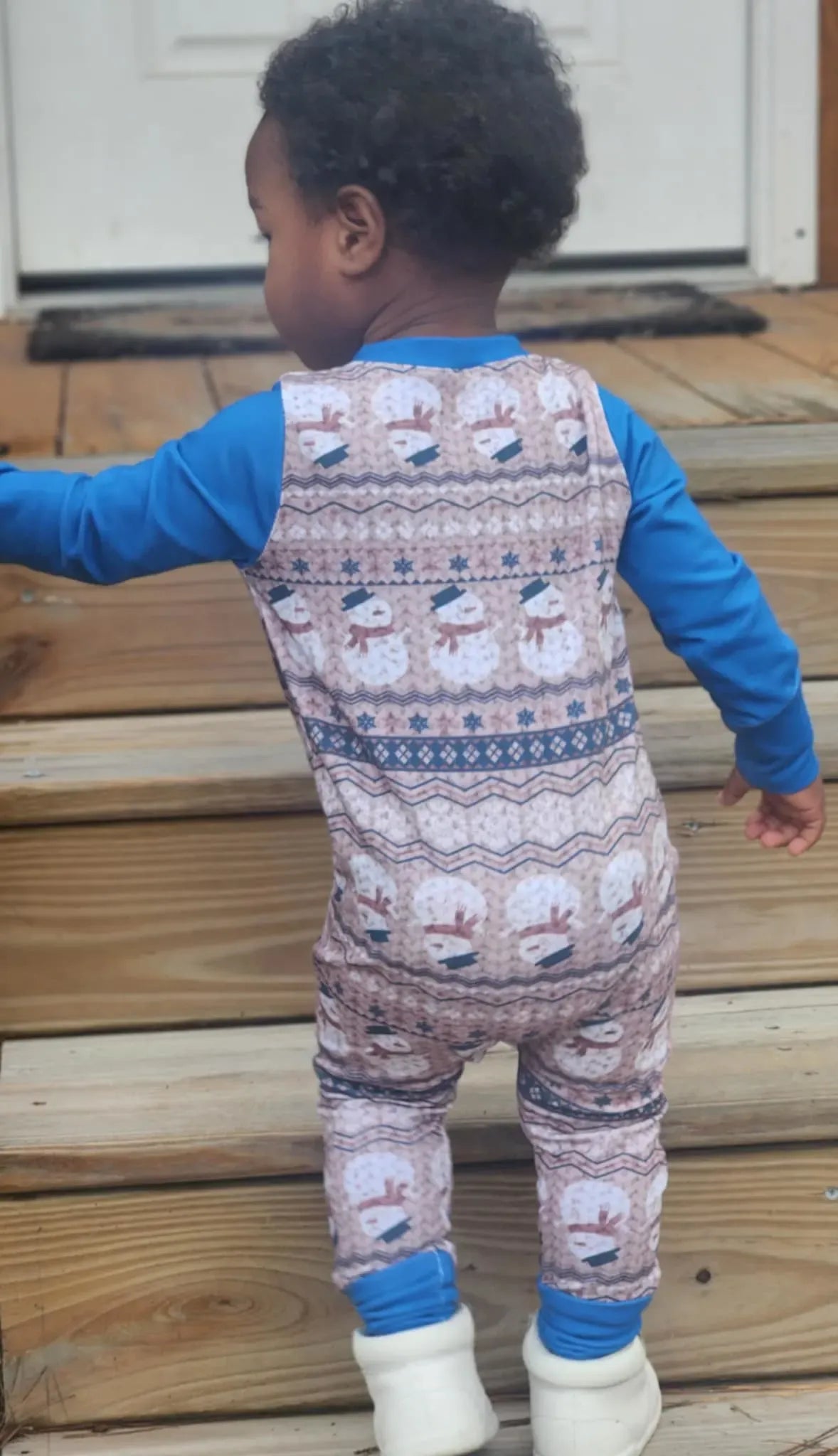 A child from behind wears a blue and white snowman-patterned long-sleeved onesie.
