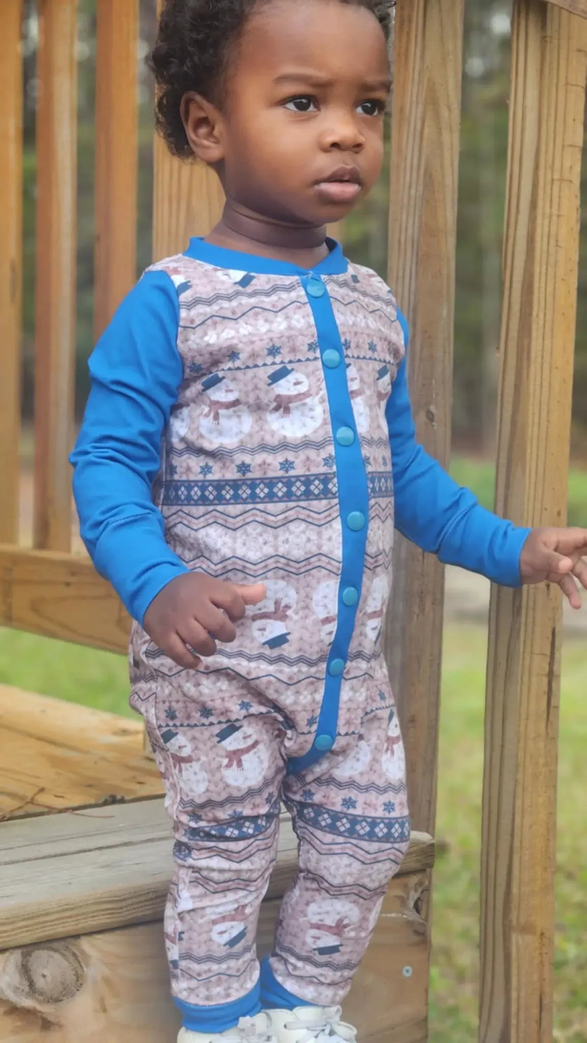 A child wears a blue and white snowman-patterned long-sleeved romper with blue snaps.