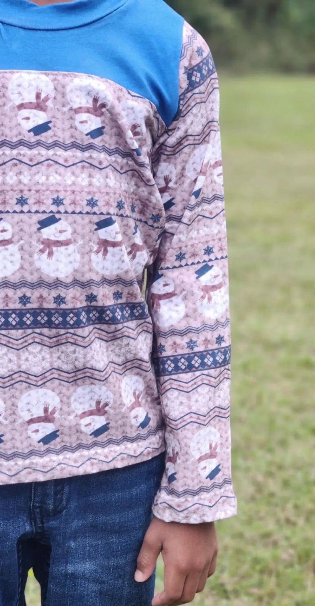 A child wears a blue and snowman-patterned long-sleeve shirt with jeans.