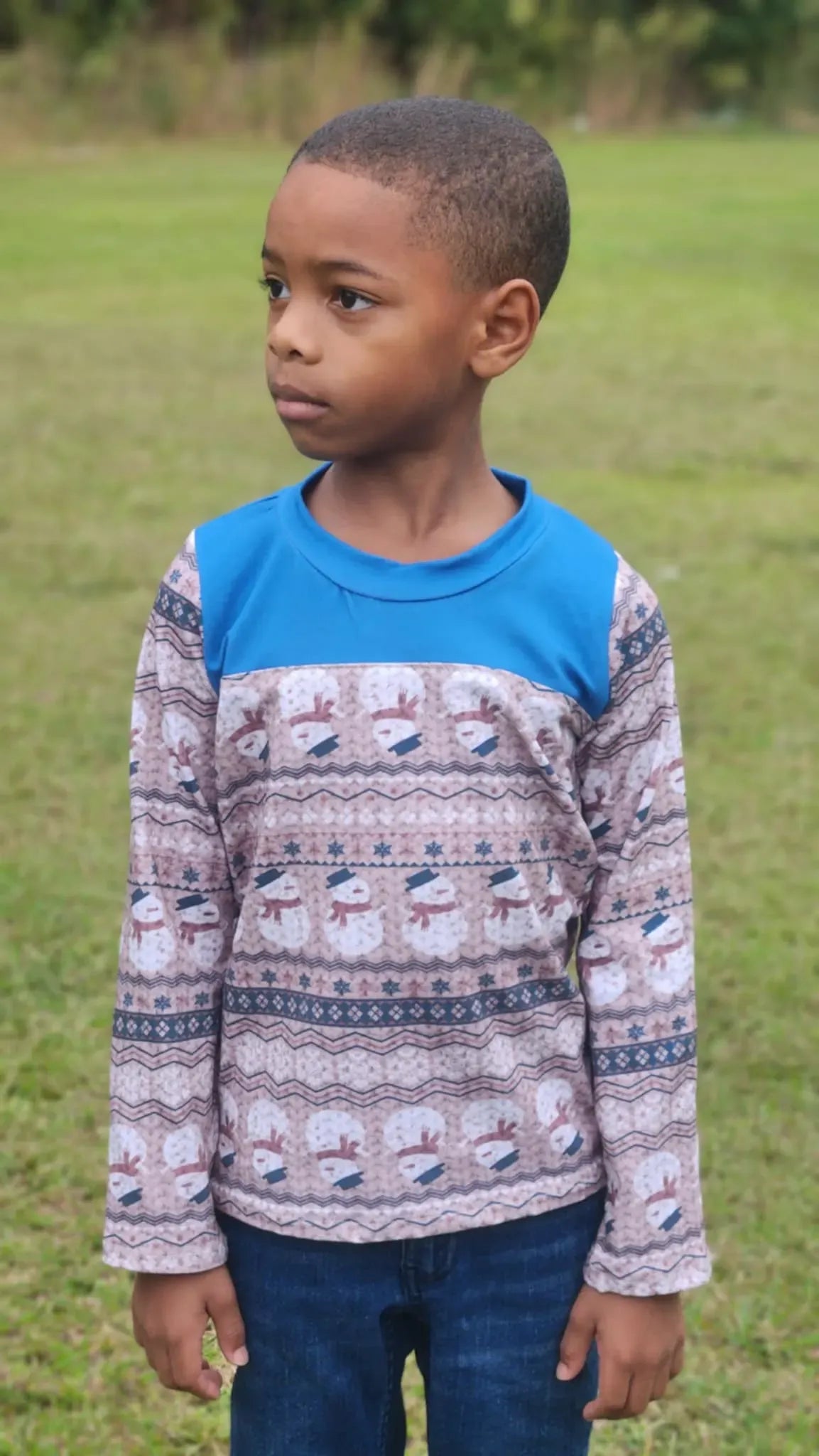 A young boy wears a long-sleeved shirt with a blue yoke and a snowman pattern.