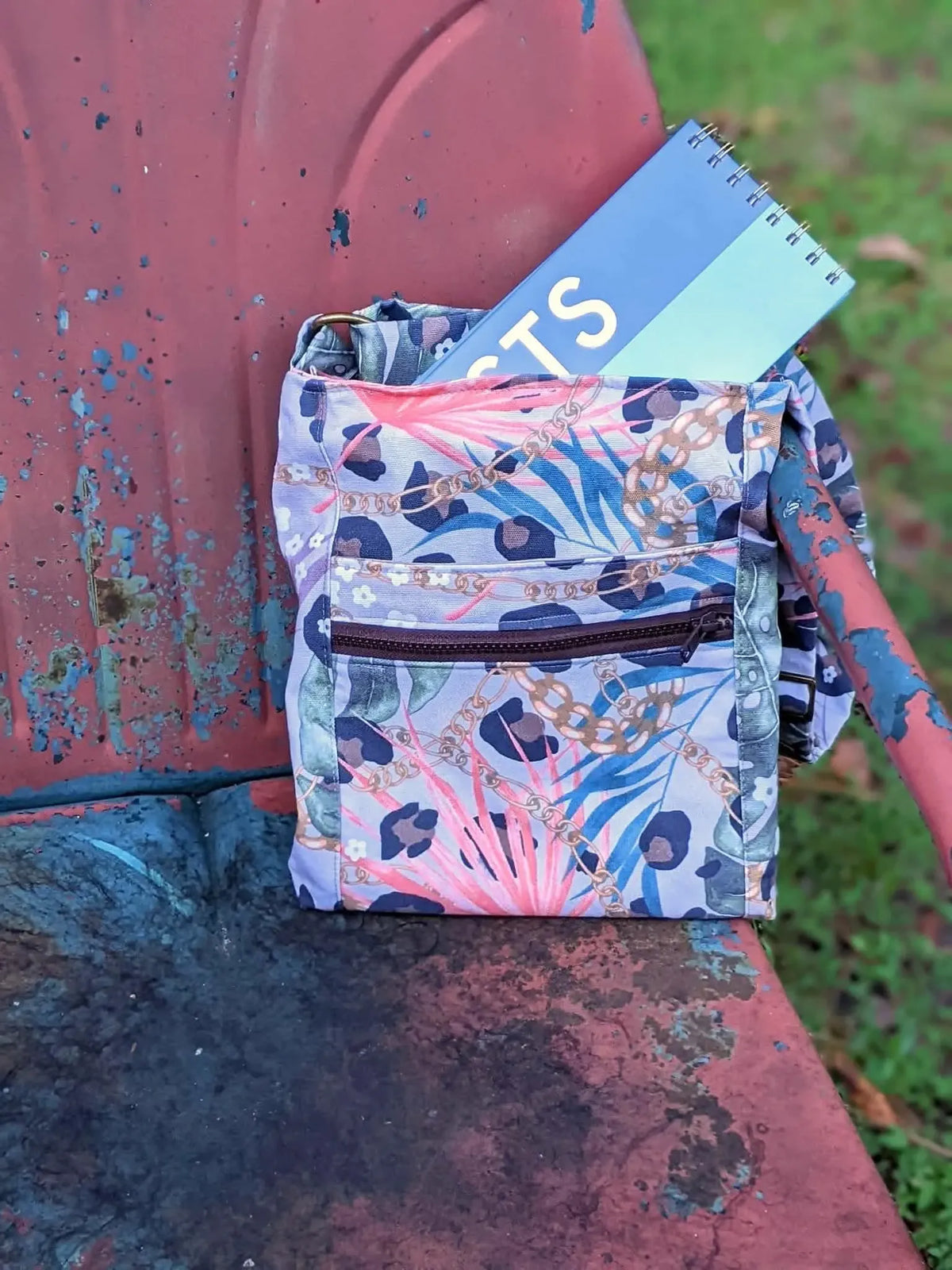 A fabric pouch with a leopard and tropical leaf print sits on a distressed red surface.
