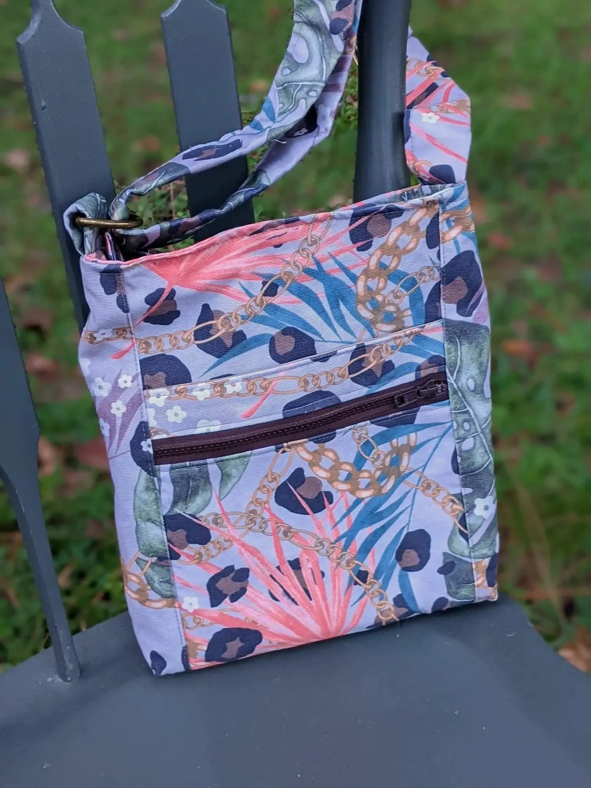 A patterned shoulder bag with leopard print, chains, and tropical leaves hangs on a chair.
