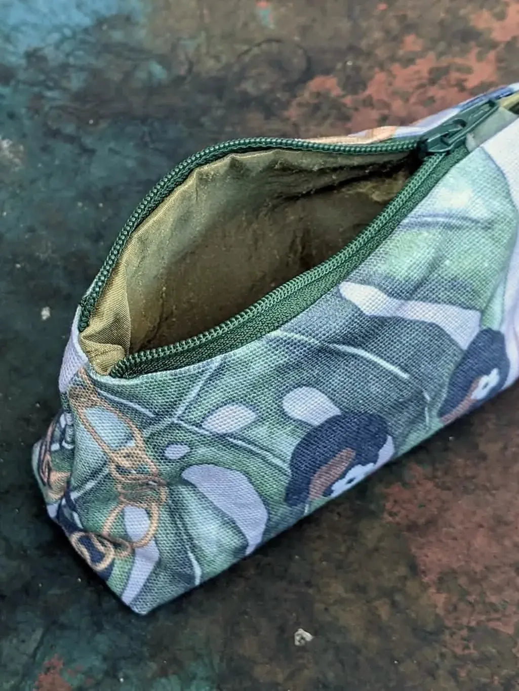 A small, open zippered pouch with a green and white leaf pattern.