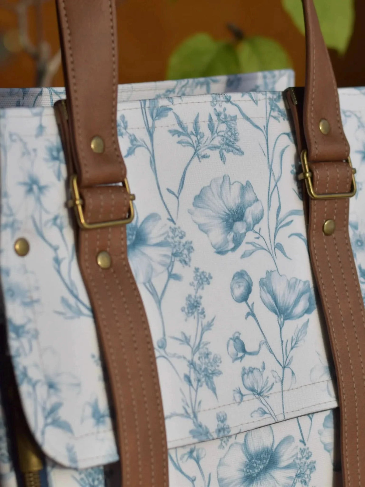 A white bag with blue floral patterns and brown leather straps.