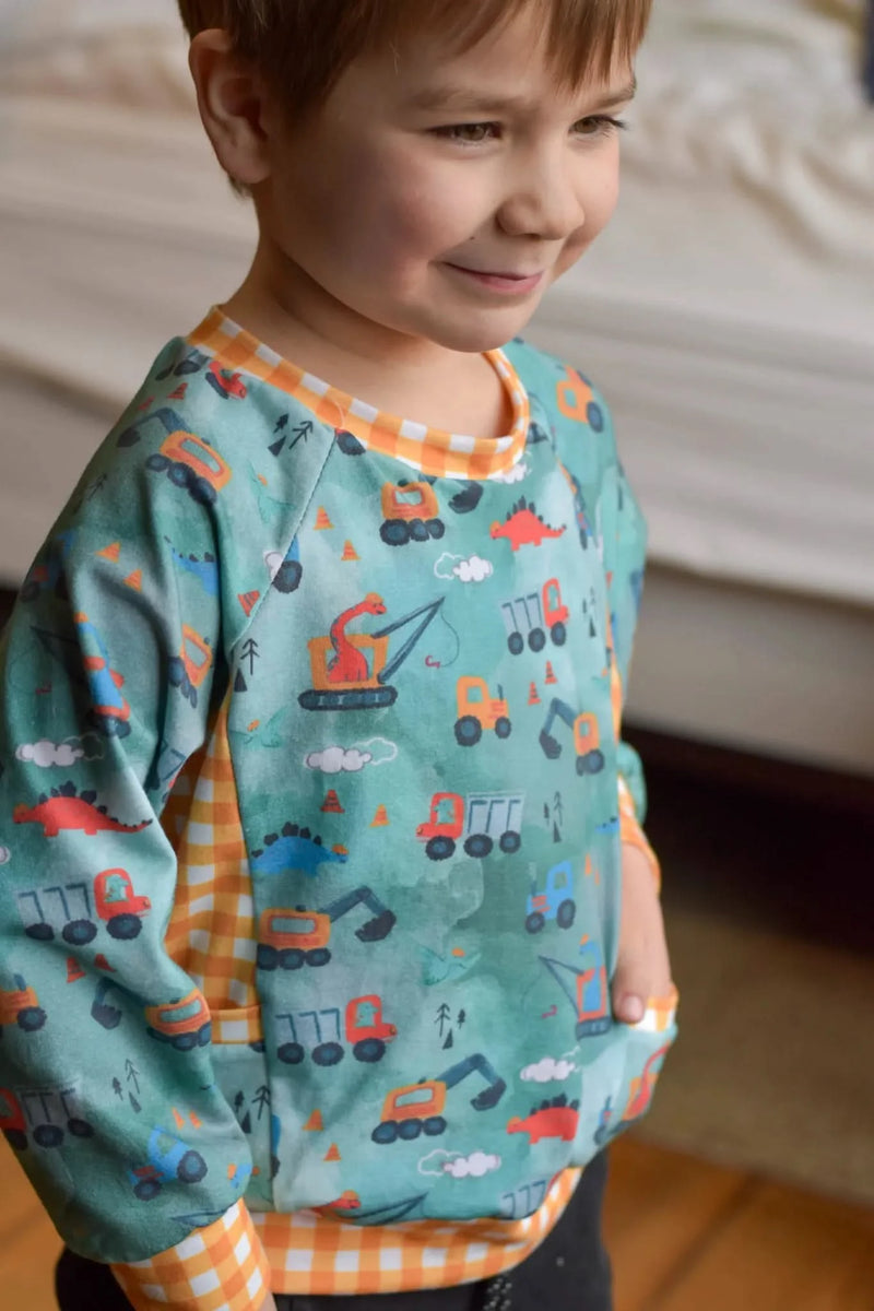 A child wears a green shirt with construction vehicles and dinosaurs.