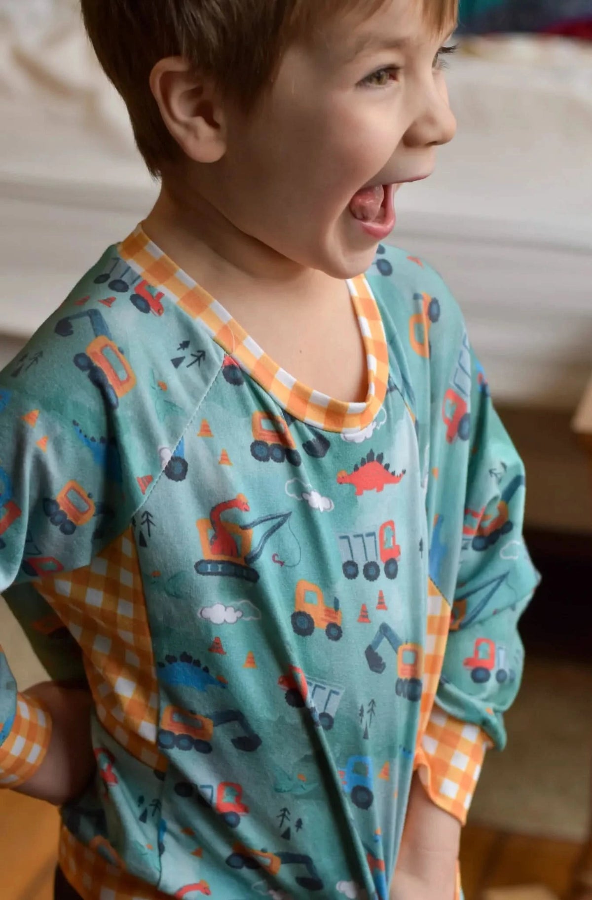 Child in a green shirt with construction vehicles and dinosaurs, and orange checkered accents.
