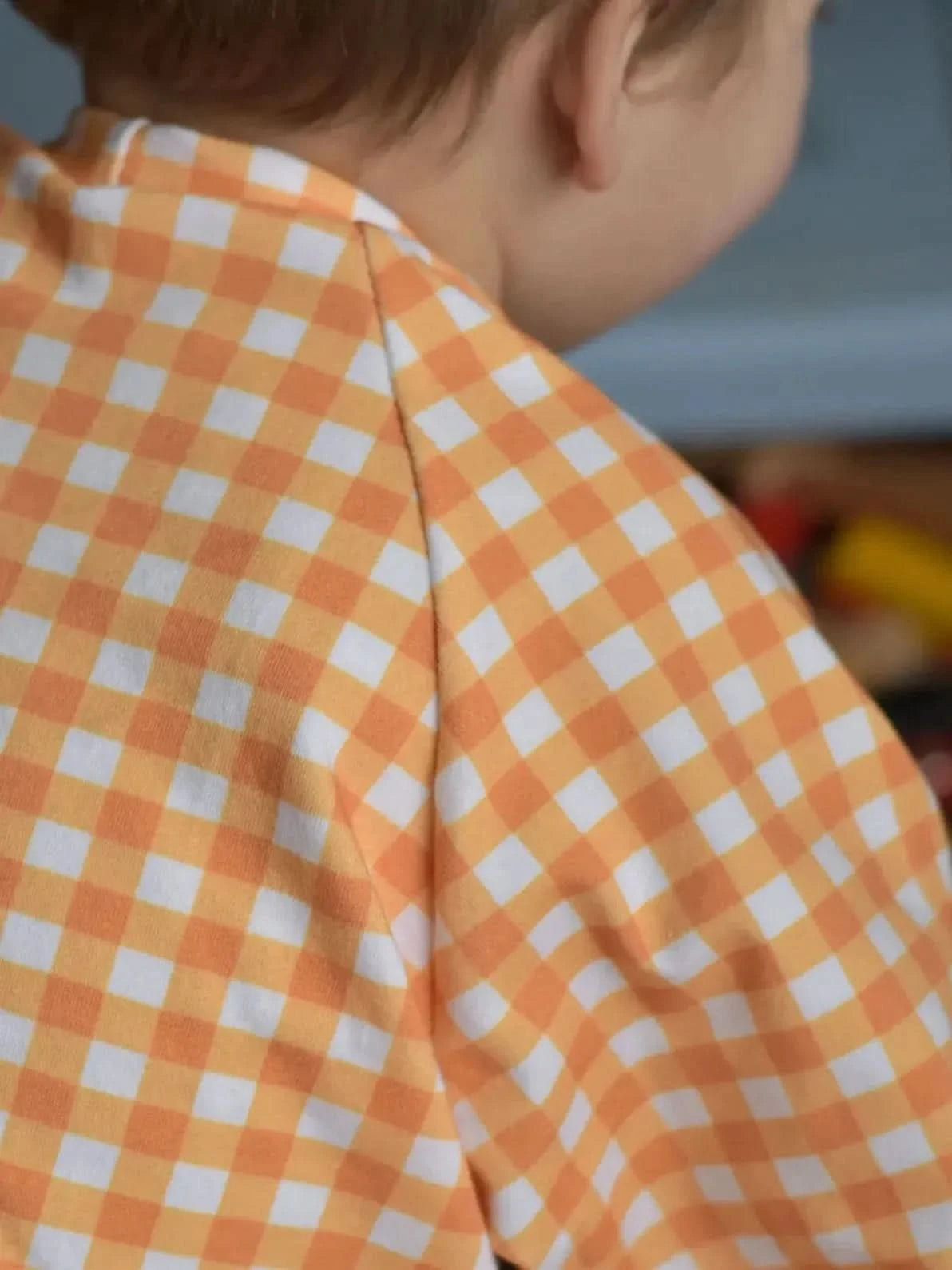 A child's back in a mustard gingham shirt.