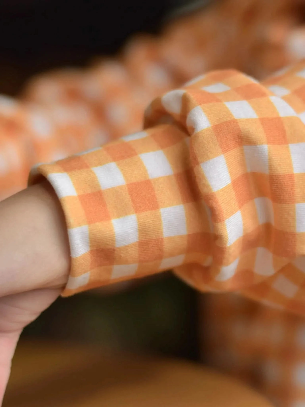 A person's arm in a mustard gingham long-sleeved shirt.