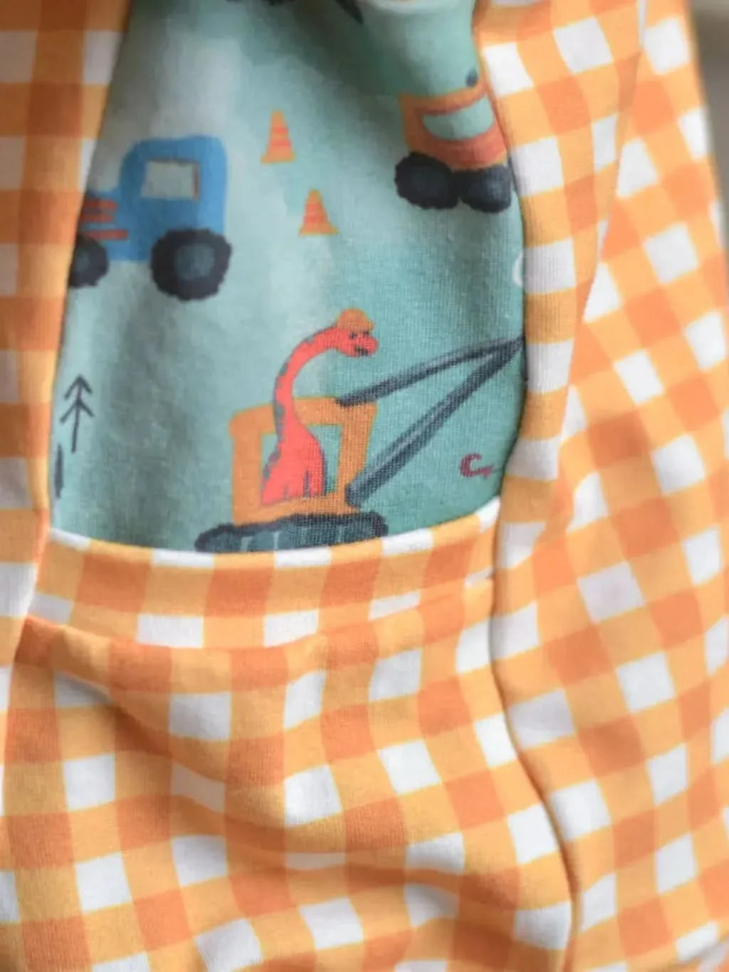 Mustard gingham fabric with a pocket featuring construction vehicles and a dinosaur.
