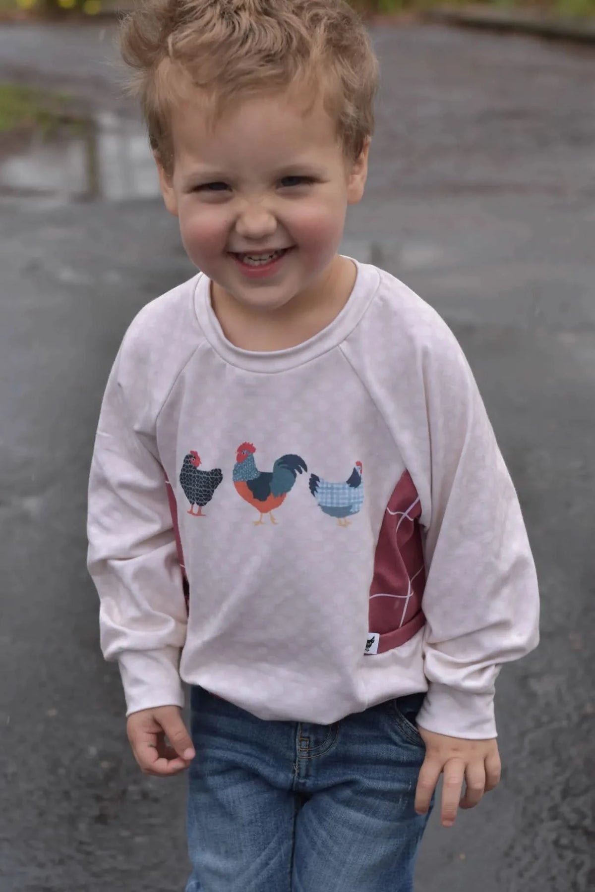 A young child wears a long-sleeved shirt with three patchwork chickens on the front.