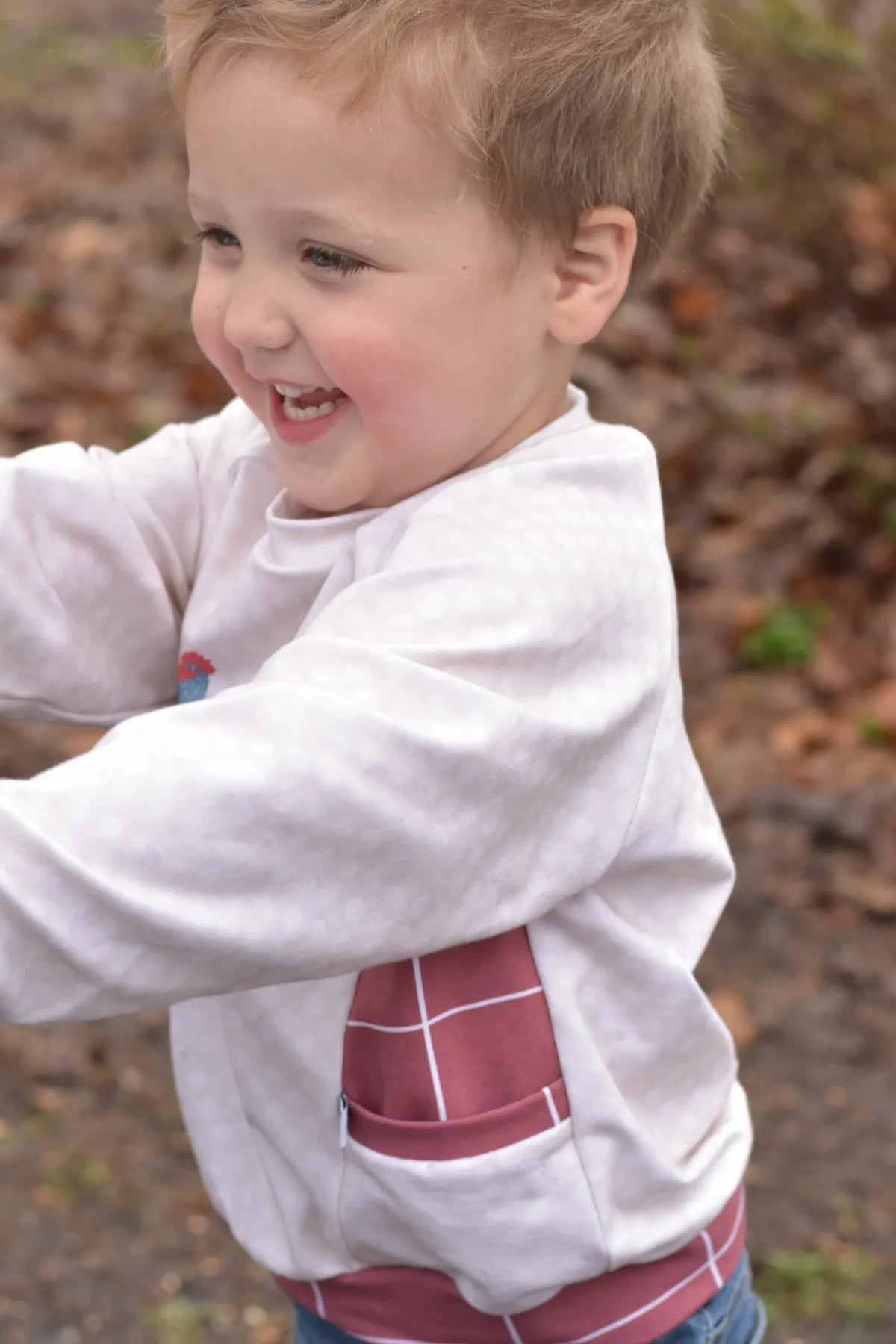 A child wears a cream shirt with a red windowpane pattern on the pocket and hem.