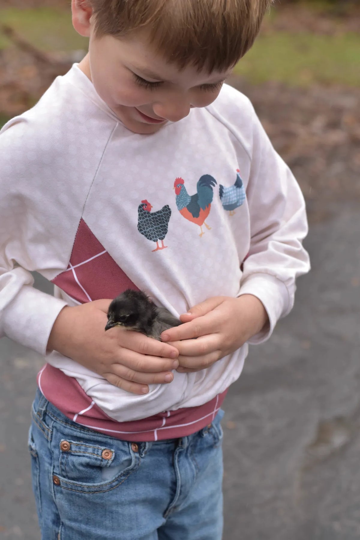 A child in a red windowpane shirt holds a small chick.